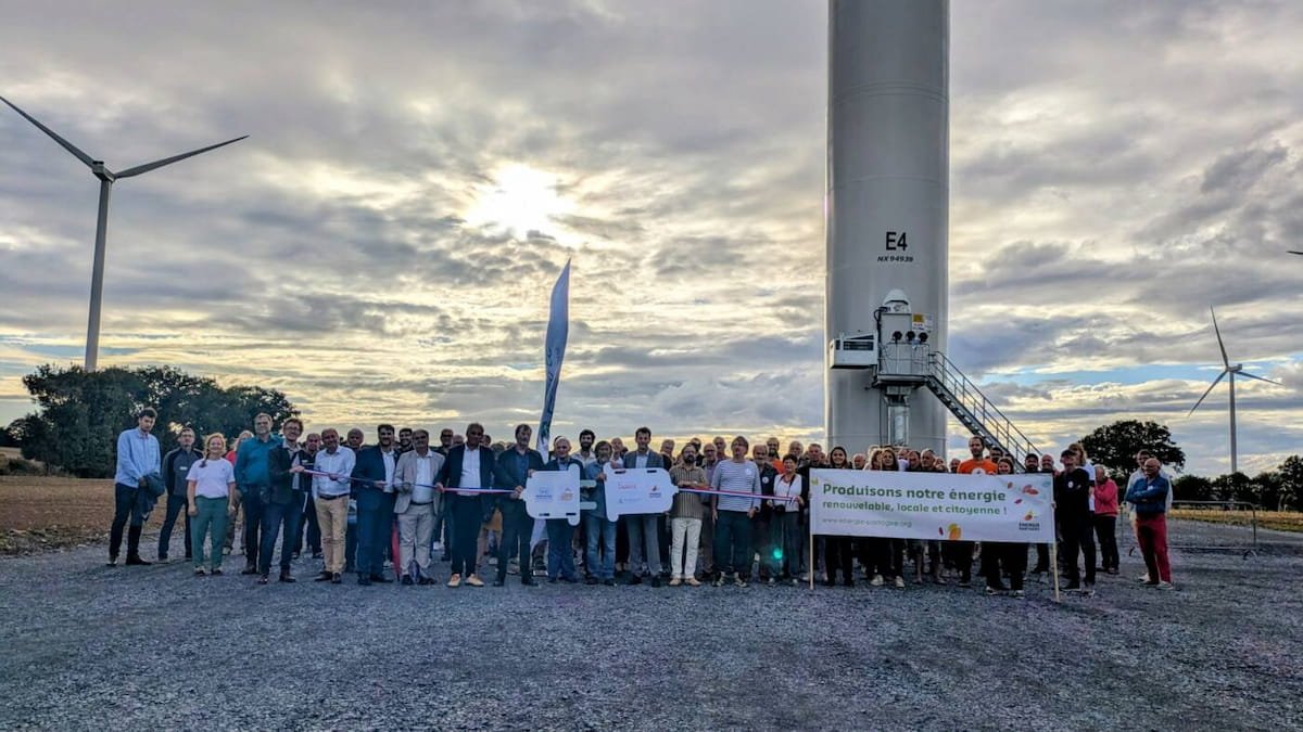 Une foule rassemblée au pied des éoliennes de Féeole, avec une prise électrique géante et une banderole "Produisons notre énergie renouvelable, locale et citoyenne"